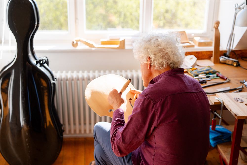 eine Person sitzt auf einem Hocker und bearbeitet einen Geigendeckel