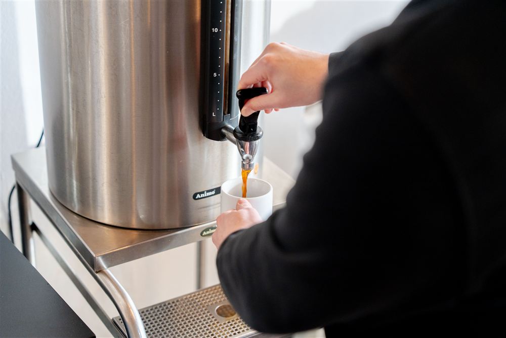 eine Person schenkt sich einen Kaffee im Speisesaal über einen Kaffeespender ein