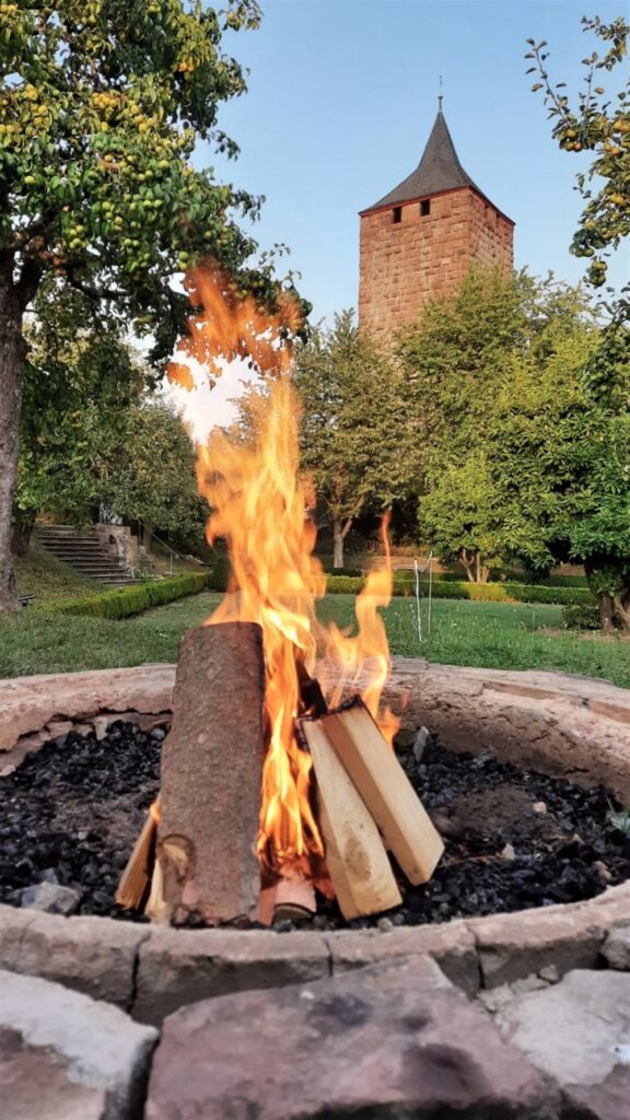 Aufnahme eines Lagerfeuers, im Hintergrund ist der Barockgarten und der Bergfried zu sehen