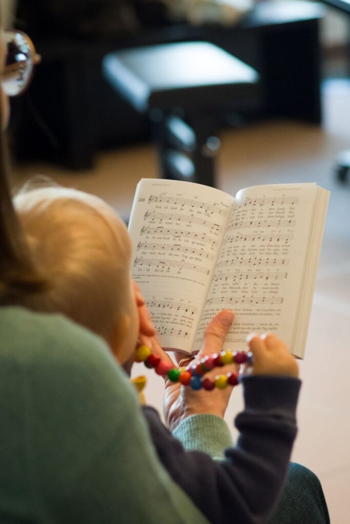Kleines Kind sitzt auf dem Schoß der Mutter und blickt zusammen mit ihr in ein Gesangbuch