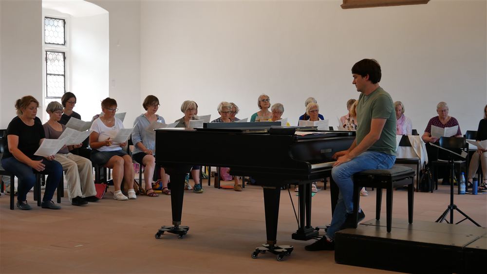 Ein Dozent der Chorwoche spiel auf dem Konzertflügel im Rittersaal, während die Teilnehmenden dazu singen
