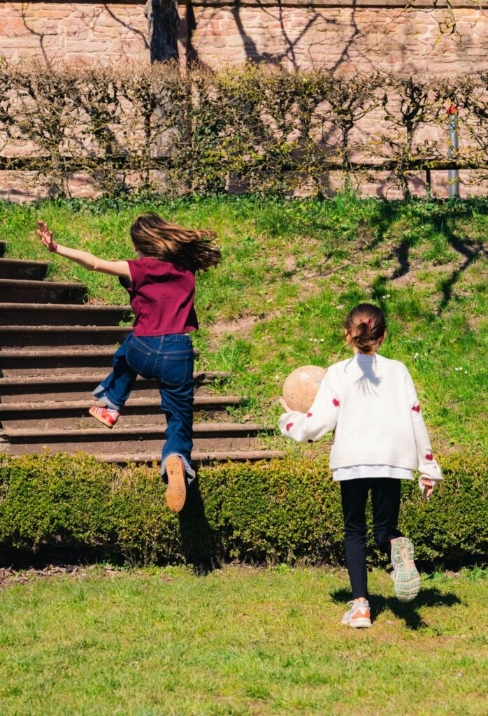 Kinder spielen auf der Wiese und springen über eine Hecke