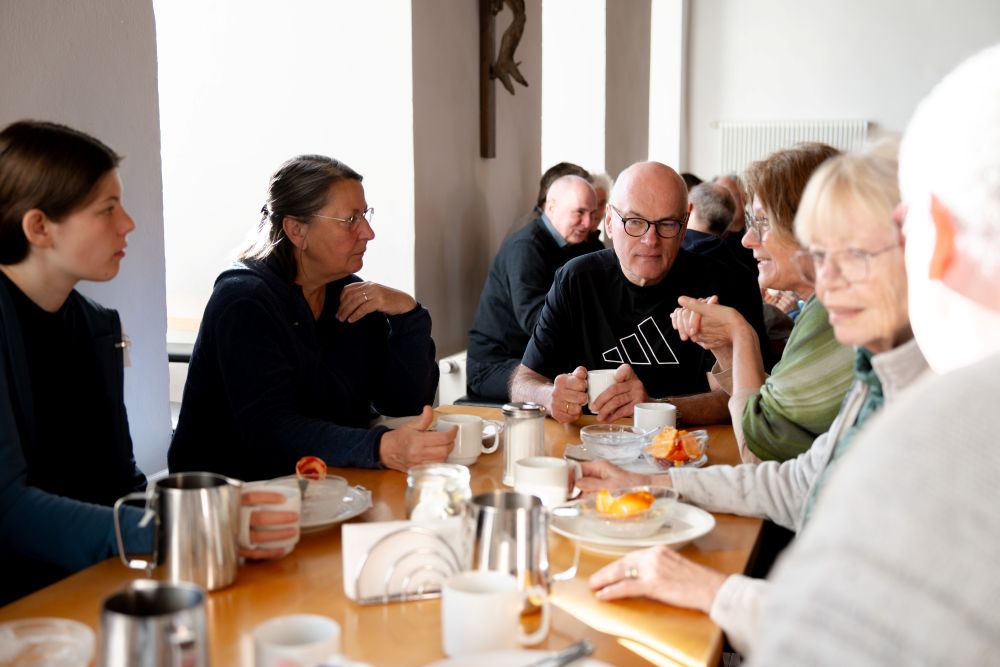Eine Gruppe Menschen sitzt beim gemeinsamen Frühstück an einem Tisch
