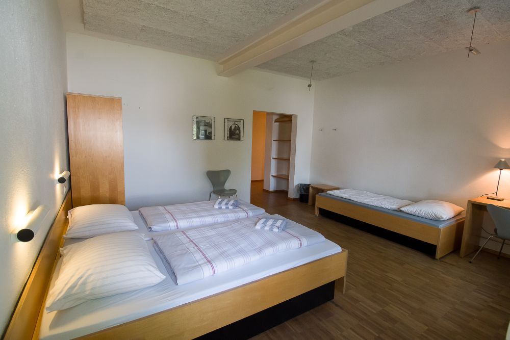 Mehrbettzimmer mit einem Doppelbett und einem einzelnen Bett. In der Ecke steht ein Kleiderschrank